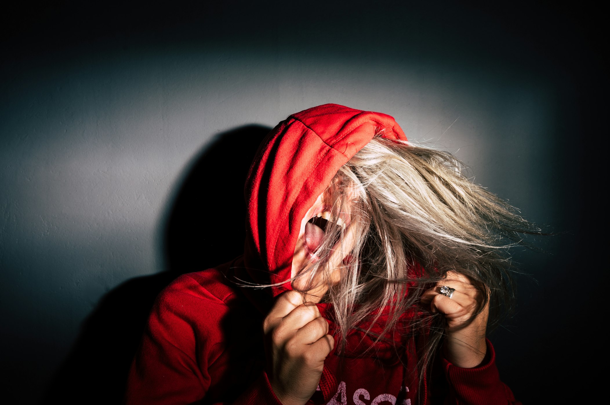 person with blonde hair wearing a red hoodie, holding hood and yelling