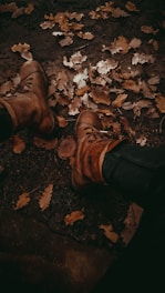A pair of elegant heeled boots displayed on a rustic wooden surface, surrounded by autumn leaves.