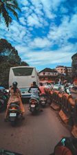 Instructor patiently guiding a learner on a motorcycle through Koramangala streets during a sunny day.