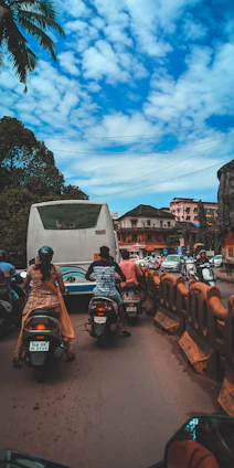 Instructor patiently guiding a learner on a motorcycle through Koramangala streets during a sunny day.