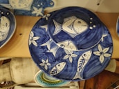 Ceramic plates with a blue and white nautical design depict fish and starfish motifs. The plates are arranged on a wooden surface, showcasing intricate patterns of marine life in a stylized form.