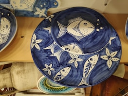Ceramic plates with a blue and white nautical design depict fish and starfish motifs. The plates are arranged on a wooden surface, showcasing intricate patterns of marine life in a stylized form.