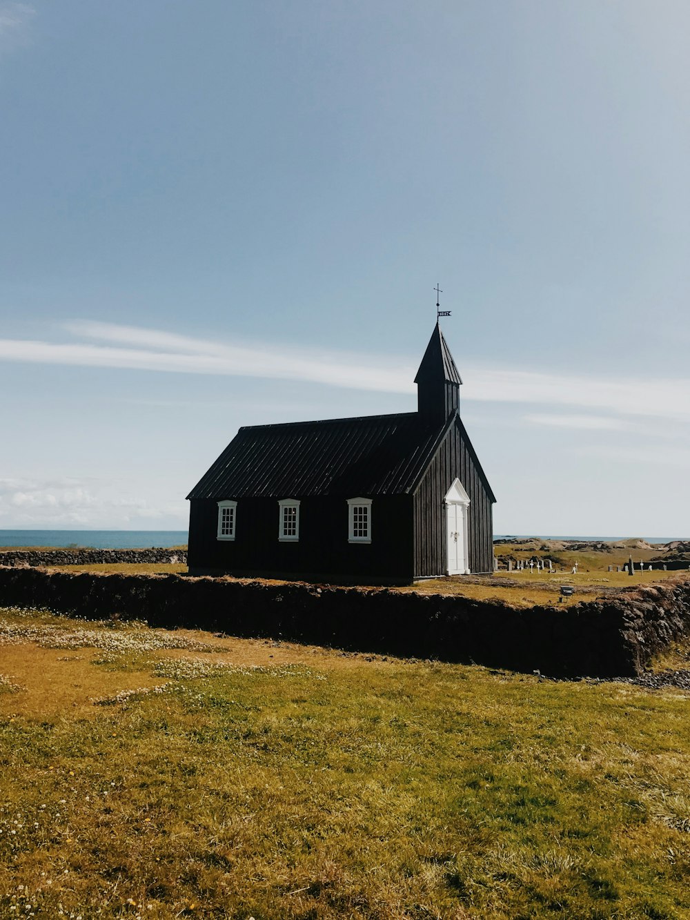 uma igreja preta com um campanário em uma colina gramada