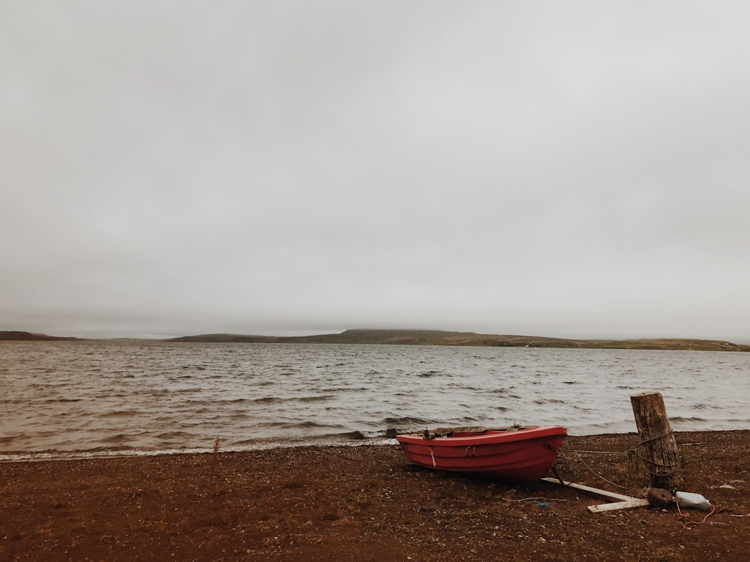 red kayak on seashore near beach during cloudy day