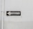 A weathered traffic sign with black text 'TRANSITO' and a left-pointing arrow is mounted against a plain, worn white wall. The sign is rectangular with a black border and white background.