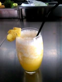 Yellow tropical pineapple and turmeric juice with a straw and pineapple slice garnish.