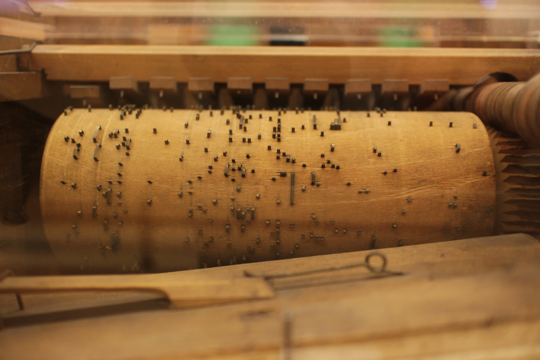 Rows of small metal pins set across the wooden barrel of a mechanical musical instrument, seen close up