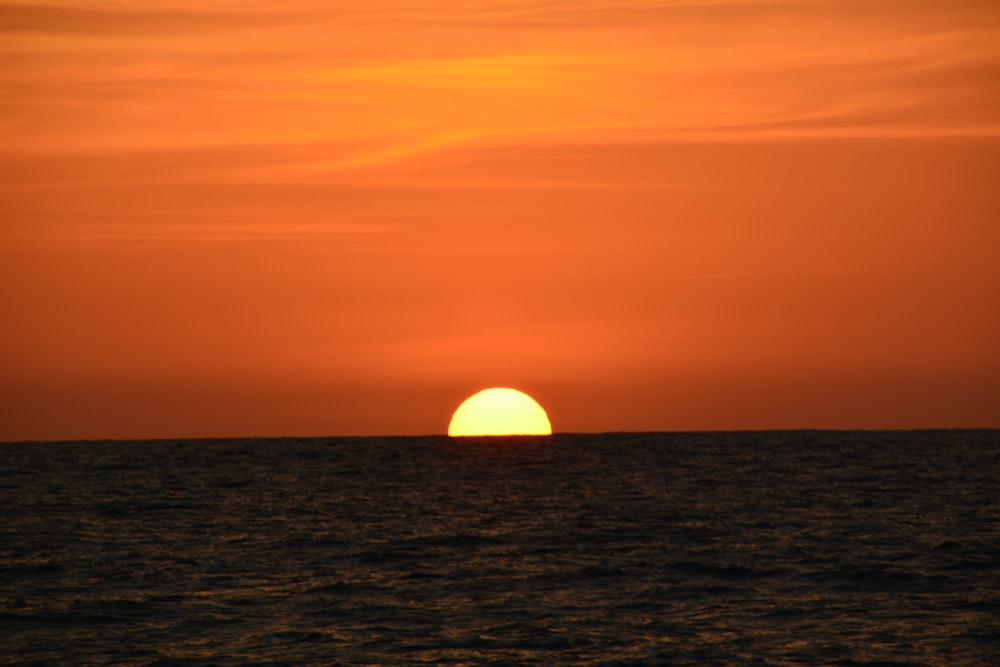 the sun is setting over the ocean on a cloudy day