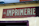 A weathered sign with the word 'IMPRIMERIE' prominently displayed in bold, serif letters on a red background. The number 46 is positioned to the left of the text. The sign is mounted on a light yellow wall, which appears to be part of an older building.