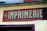 A weathered sign with the word 'IMPRIMERIE' prominently displayed in bold, serif letters on a red background. The number 46 is positioned to the left of the text. The sign is mounted on a light yellow wall, which appears to be part of an older building.