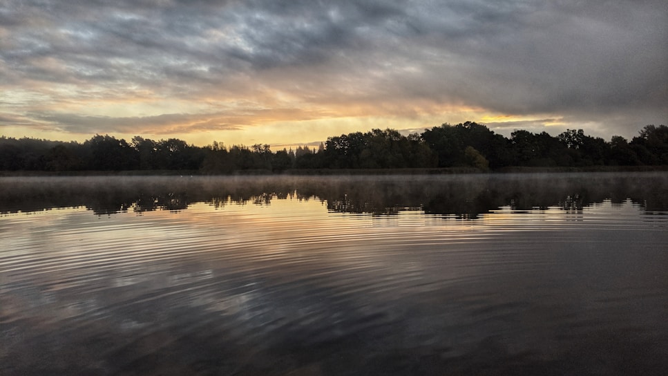 A serene landscape with a sunrise illuminating a calm lake.