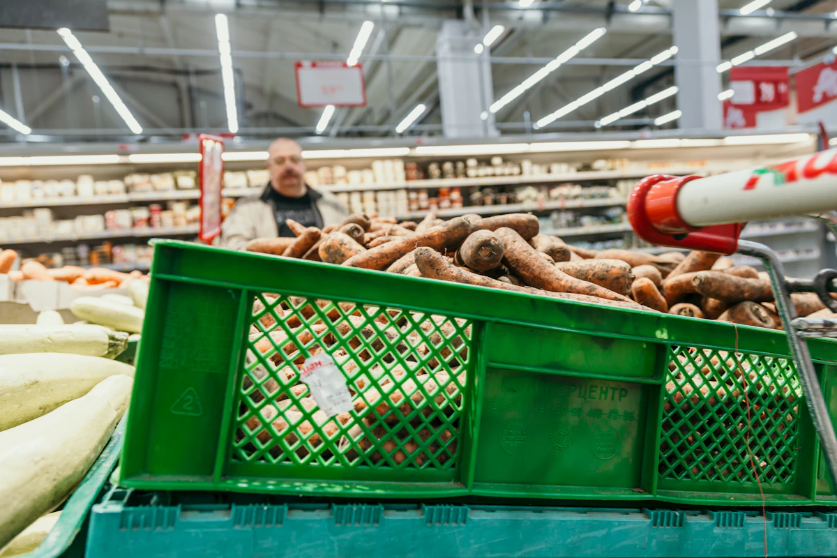 Caisses vertes de légumes dans l'allée d'un supermarché, un employé en arrière-plan