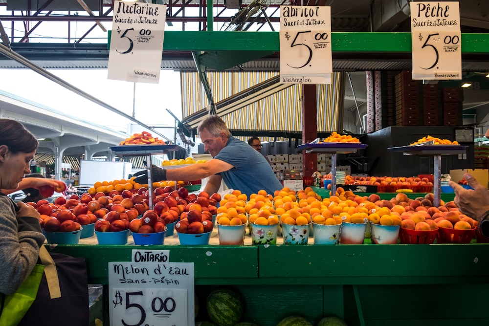 man in blue top standing beside bunch of fruits