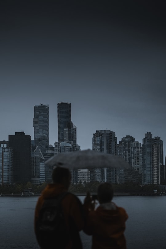 man wearing orange jacket using gray umbrella in Stanley Park Canada