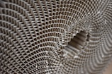 A close-up view of a corrugated cardboard material, showcasing its intricate honeycomb-like pattern. The image highlights the symmetrical, repetitive structure of the corrugated layers, creating a sense of depth and texture.