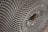 A close-up view of a corrugated cardboard material, showcasing its intricate honeycomb-like pattern. The image highlights the symmetrical, repetitive structure of the corrugated layers, creating a sense of depth and texture.