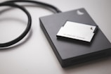 A solid-state drive is connected by a black cable, accompanied by a 256GB AV PRO CF card placed on top. The objects rest on a smooth, light-colored surface.