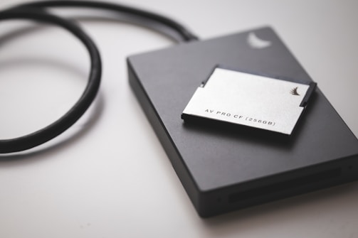 A solid-state drive is connected by a black cable, accompanied by a 256GB AV PRO CF card placed on top. The objects rest on a smooth, light-colored surface.
