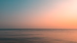 View of the calm sea horizon at sunset with soft pastel colors.