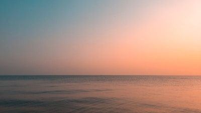 View of the calm sea horizon at sunset with soft pastel colors.