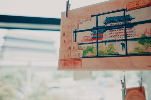 A detailed watercolor painting of a traditional Asian pagoda with green and red accents is clipped and displayed against a softly blurred background. The scene outside the window is reminiscent of the depicted architecture, suggesting a connection between the artwork and its surroundings.