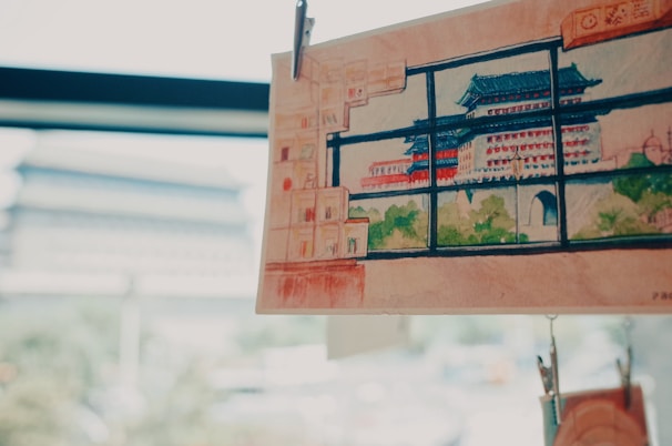 A detailed watercolor painting of a traditional Asian pagoda with green and red accents is clipped and displayed against a softly blurred background. The scene outside the window is reminiscent of the depicted architecture, suggesting a connection between the artwork and its surroundings.
