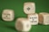 A close-up view of wooden dice with playing card suit symbols and numbers on their faces, resting on a green felt surface.