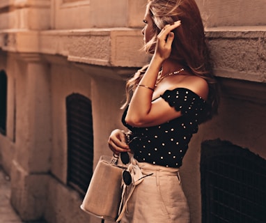 woman wearing black blouse and white short-shorts carrying bag leaning on wall