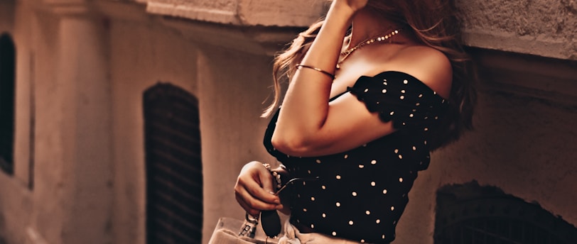 woman wearing black blouse and white short-shorts carrying bag leaning on wall