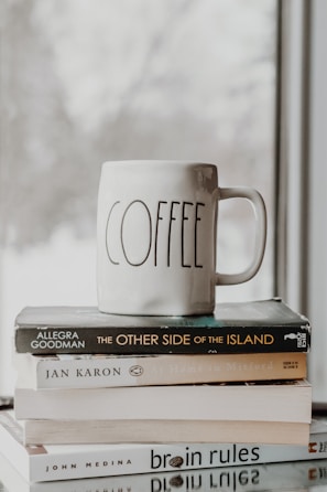 A white coffee mug with a cheerful custom message and bright graphics, sitting beside a stack of books.