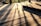 Wooden decking is bathed in warm sunlight, casting long, defined shadows from vertical beams. The light creates a pattern on the textured surface, adding depth and dimension to the scene.