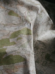 A detailed topographical map with green, blue, and brown areas indicating various terrain features such as forests, rivers, and elevations. The map is slightly crumpled, adding a textured appearance.