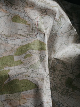 A detailed topographical map with green, blue, and brown areas indicating various terrain features such as forests, rivers, and elevations. The map is slightly crumpled, adding a textured appearance.