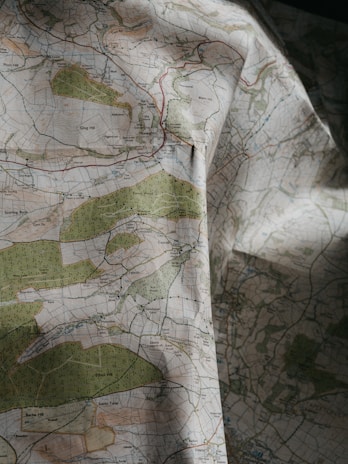 A detailed topographical map with green, blue, and brown areas indicating various terrain features such as forests, rivers, and elevations. The map is slightly crumpled, adding a textured appearance.