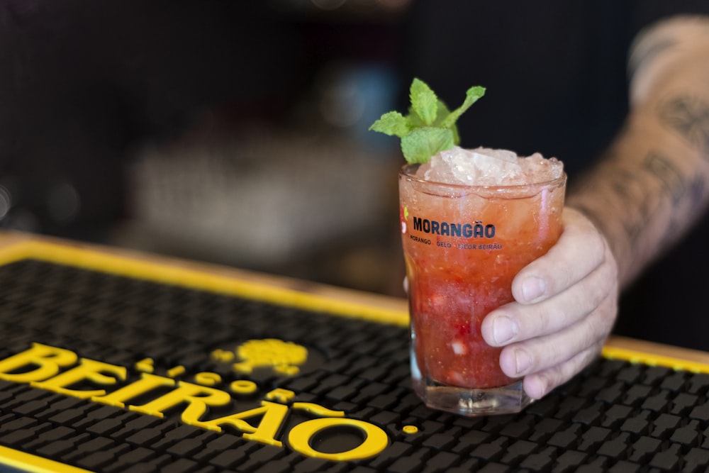 selective focus photo of man holding glass of strawberry juice full of ice