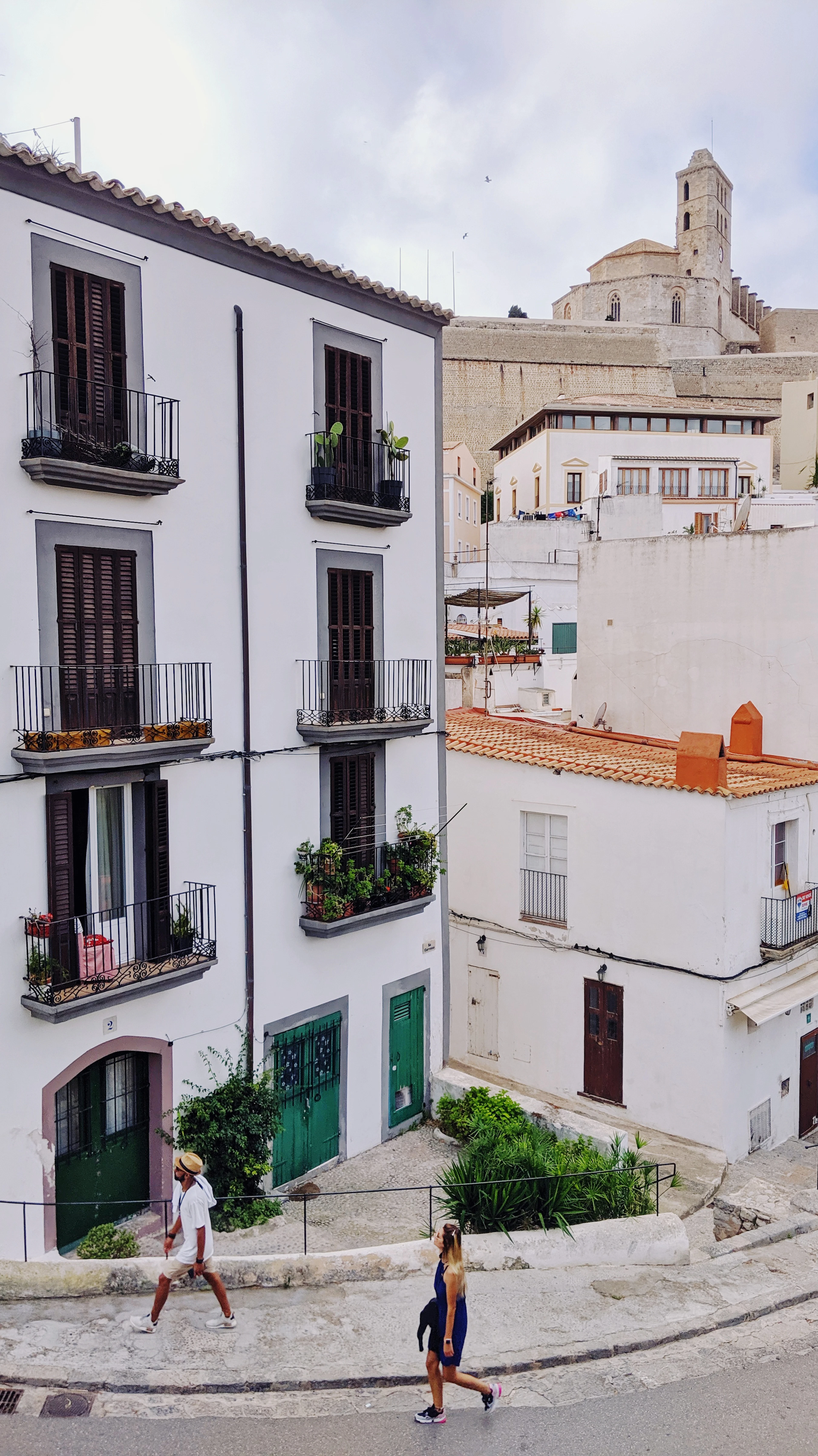 Whitewashed houses with shuttered balconies climbing the hill of Dalt Vila, Ibiza's walled old town, with the pale bell tower of the cathedral on the ridge above
