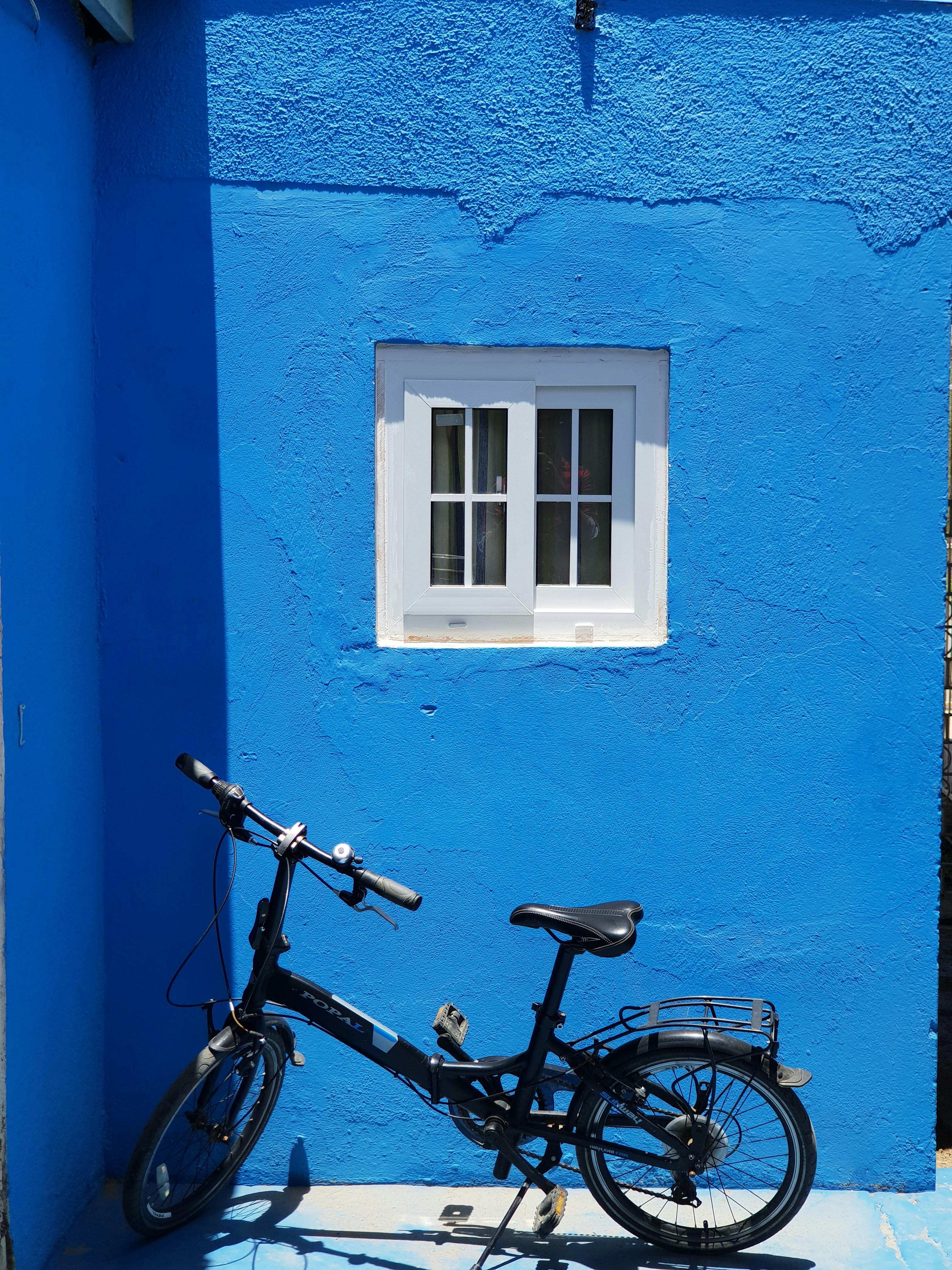 Blue hybrid bicycle against white wall, clean minimal setting, natural daylight
