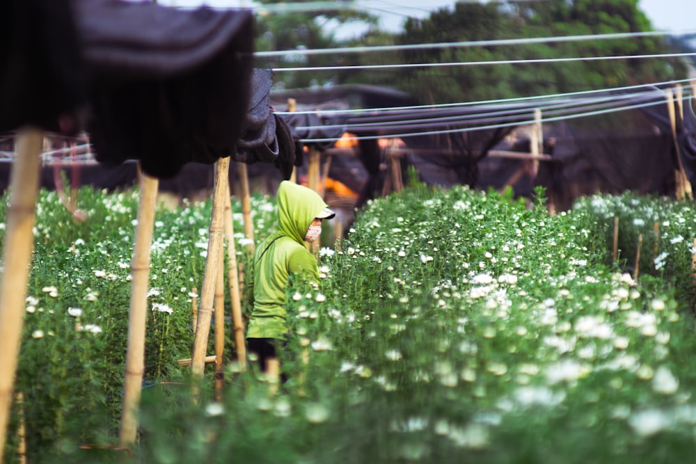 person wearing green hooded shirt standing near flower garden during daytime