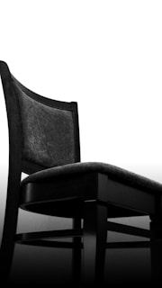 A modern, minimalist chair with a black frame and a dark cushioned seat. The backrest is slightly curved, adding a touch of elegance, and the overall design is sleek and contemporary.