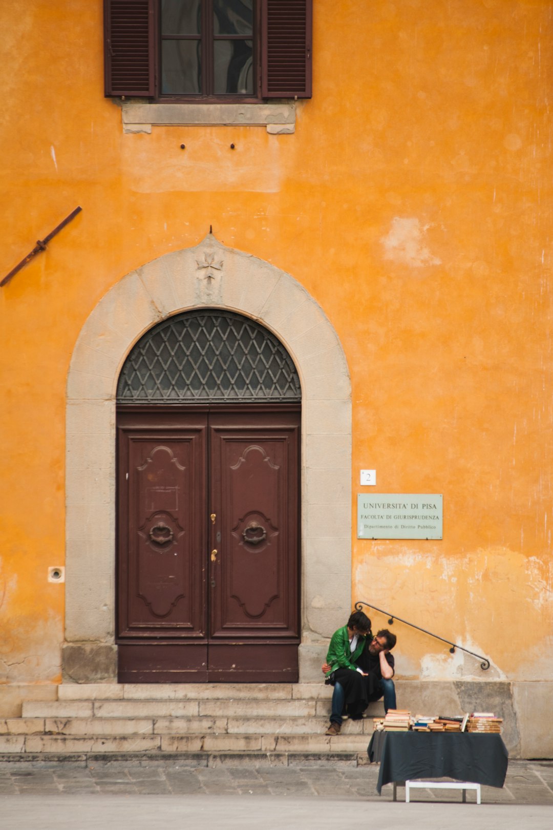 two persons sitting on stairs beside closed French doors during day