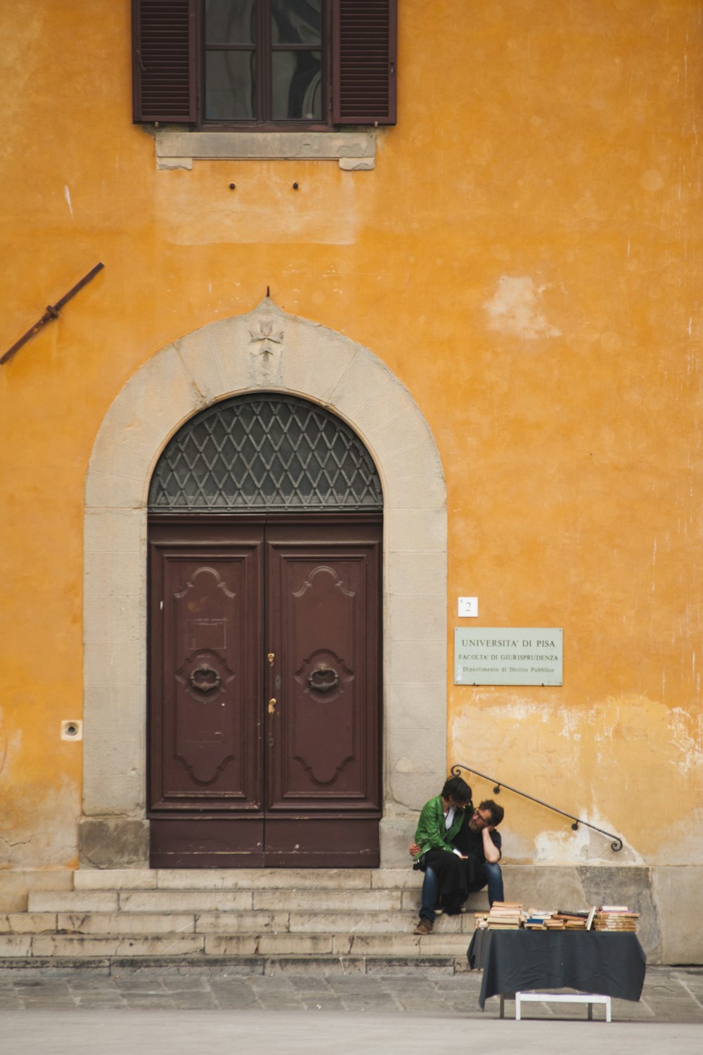 two persons sitting on stairs beside closed French doors during day