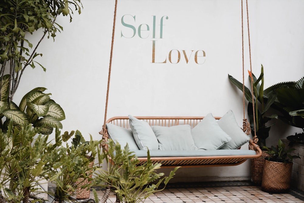 Self Love written on wall over swing with potted plants around