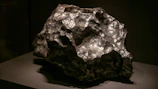 Handheld earthy meteorite with warm ivory highlights on dark navy fabric.