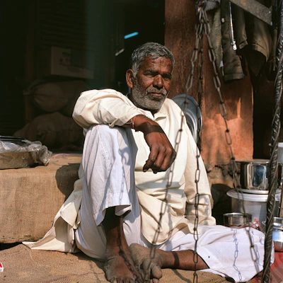 A candid photo of an elderly man standing barefoot on a sunlit wooden floor, embodying raw simplicity.