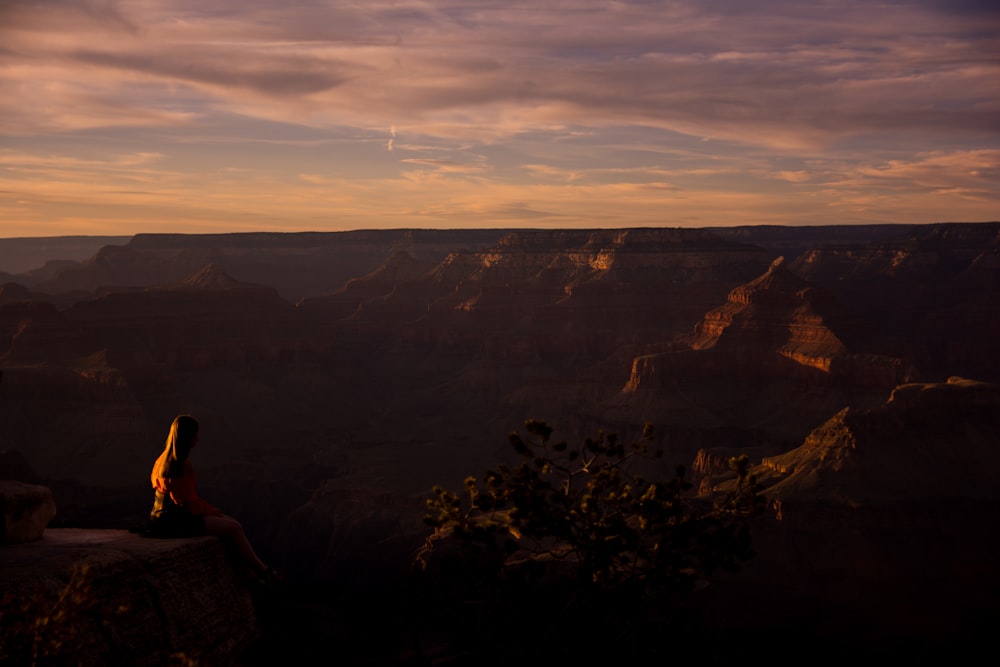 woman sitting on cliff during sunset