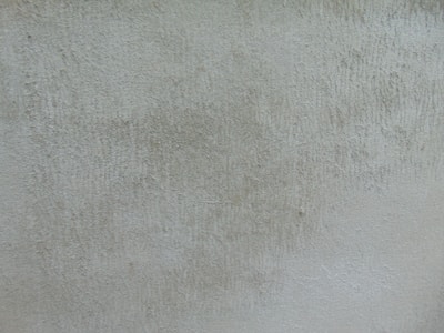A textured surface with a rough, uneven look, featuring subtle variations in color and depth. The texture resembles old concrete or plaster with visible marks and irregularities.
