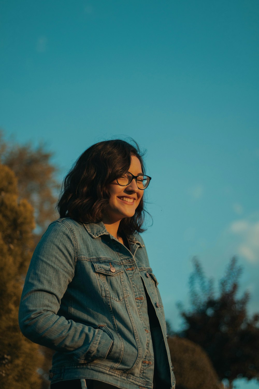 woman wearing blue denim jacket and eyeglasses standing and laughing