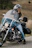 A rider adjusting their helmet beside a classic Indian motorcycle on a scenic route.