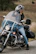 A rider adjusting their helmet beside a classic Indian motorcycle on a scenic route.