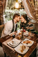 Close-up of a couple holding hands over a breakfast tray filled with croissants, strawberries, and a small bouquet.